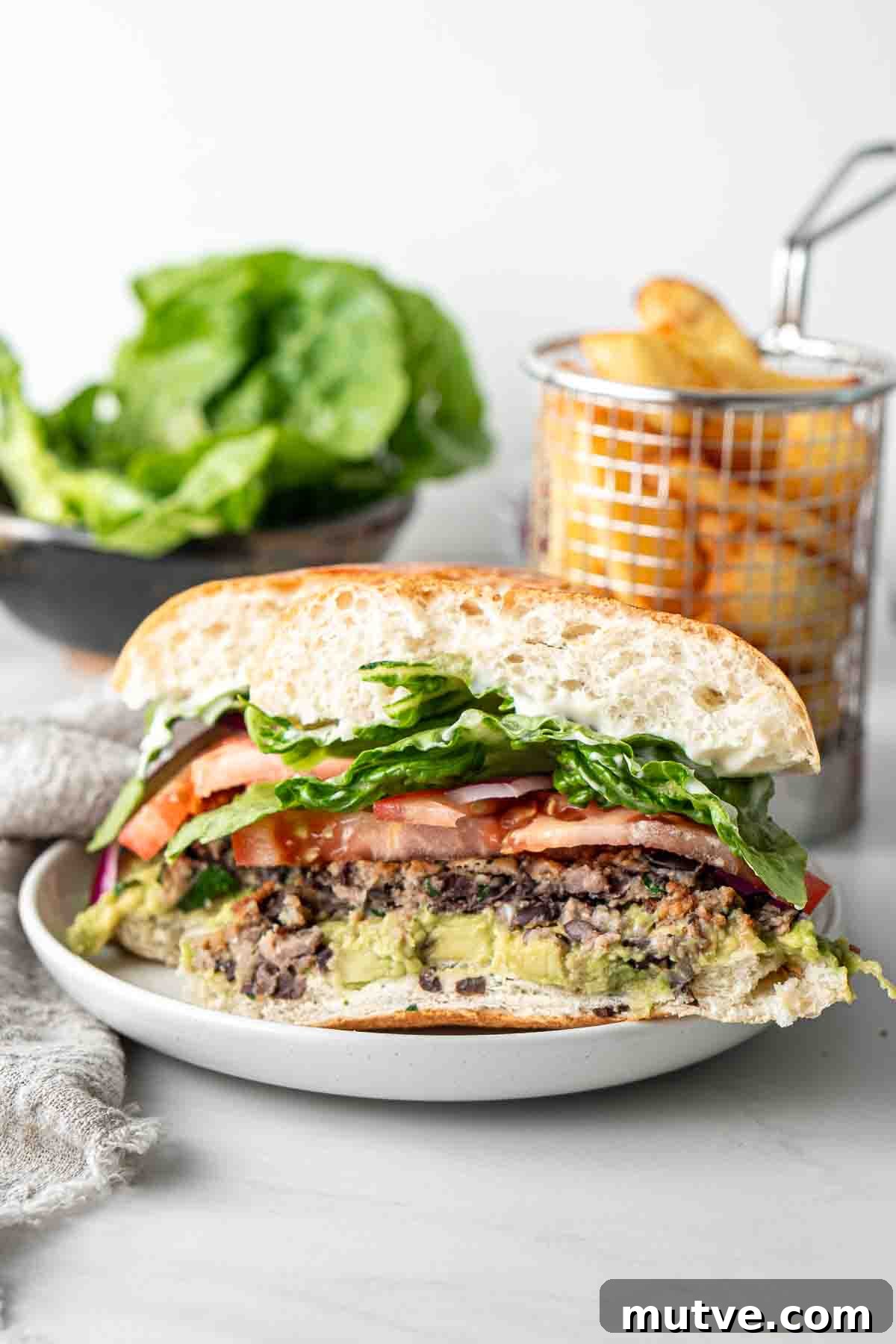 Close up of a black bean burger cut in half showing the layers with chips and salad in the background. 
