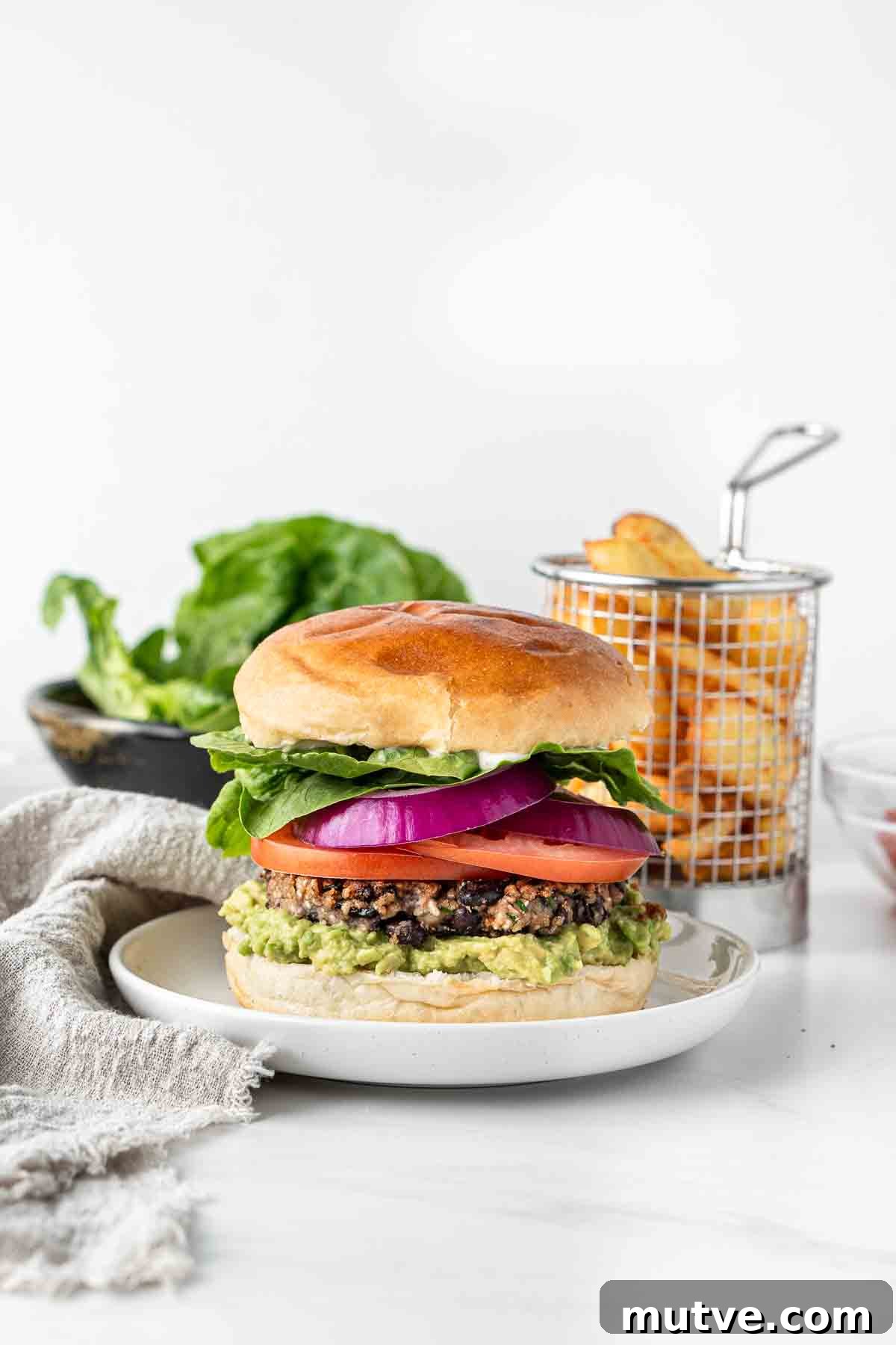 Vegan black bean burger on a plate with chips and salad in the background.