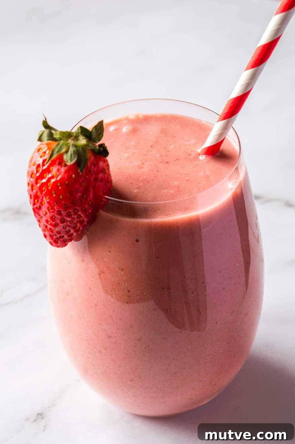 How to Start a Food Blog and Monetize It 4 Front view of a round glass with a pink smoothie, a strawberry on the rim, and a red and white paper straw