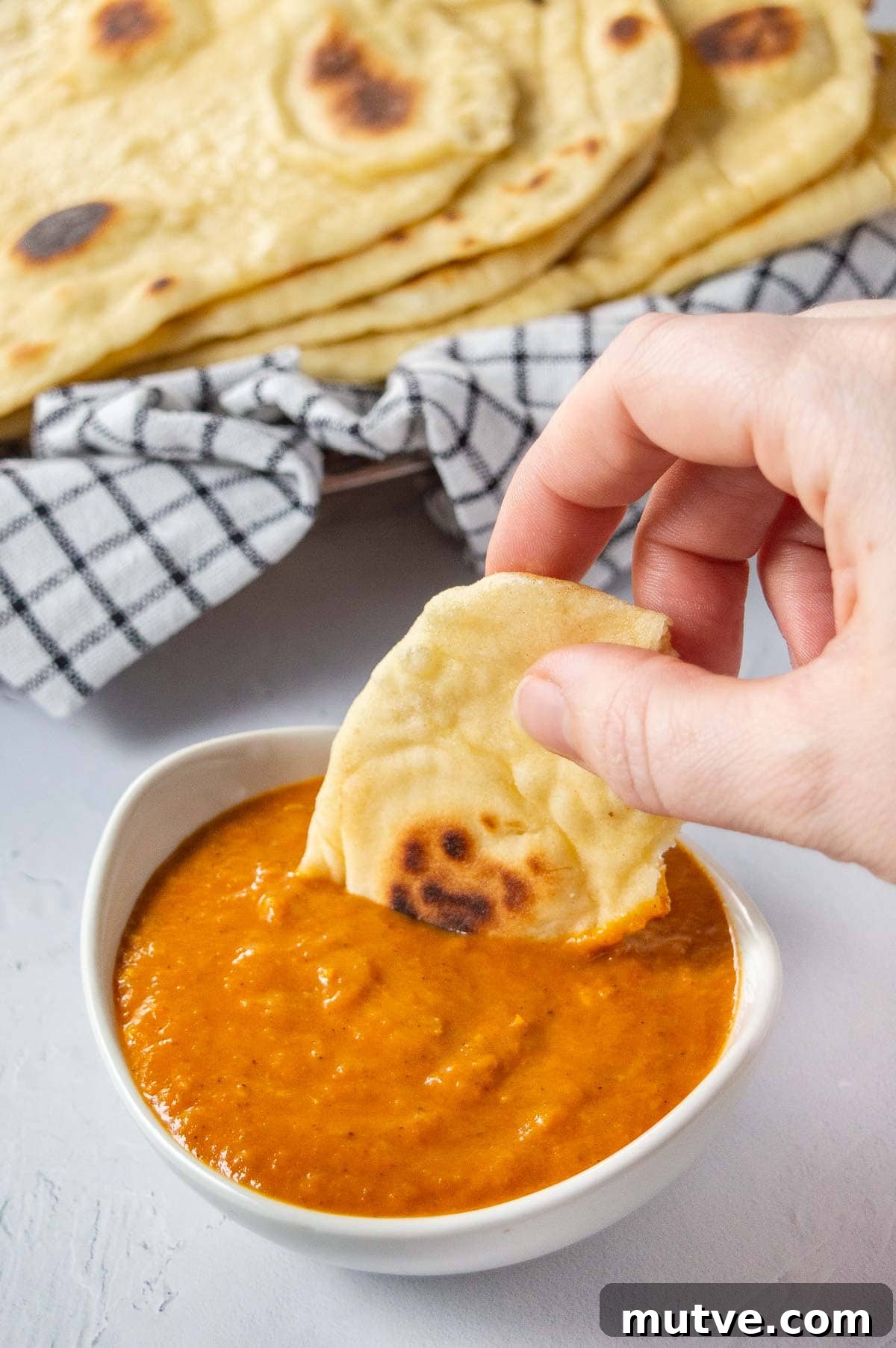 How to Start a Food Blog and Monetize It 5 A hand dipping piece of naan bread into a small white bowl of orange sauce.