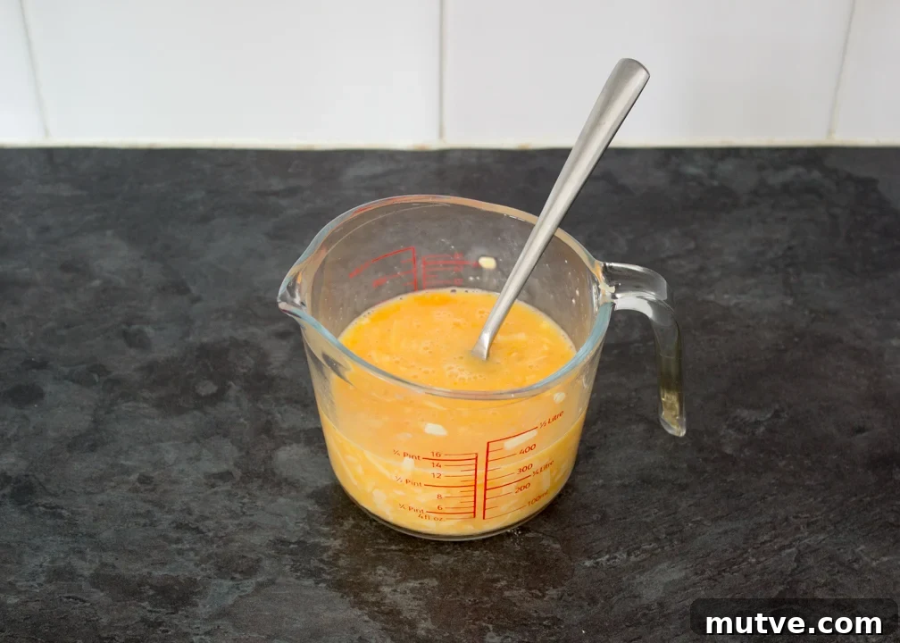 Cheese and Chive Scrambled Egg Croissant Recipe 11 Beaten egg, milk and cheese in a jug with a fork.