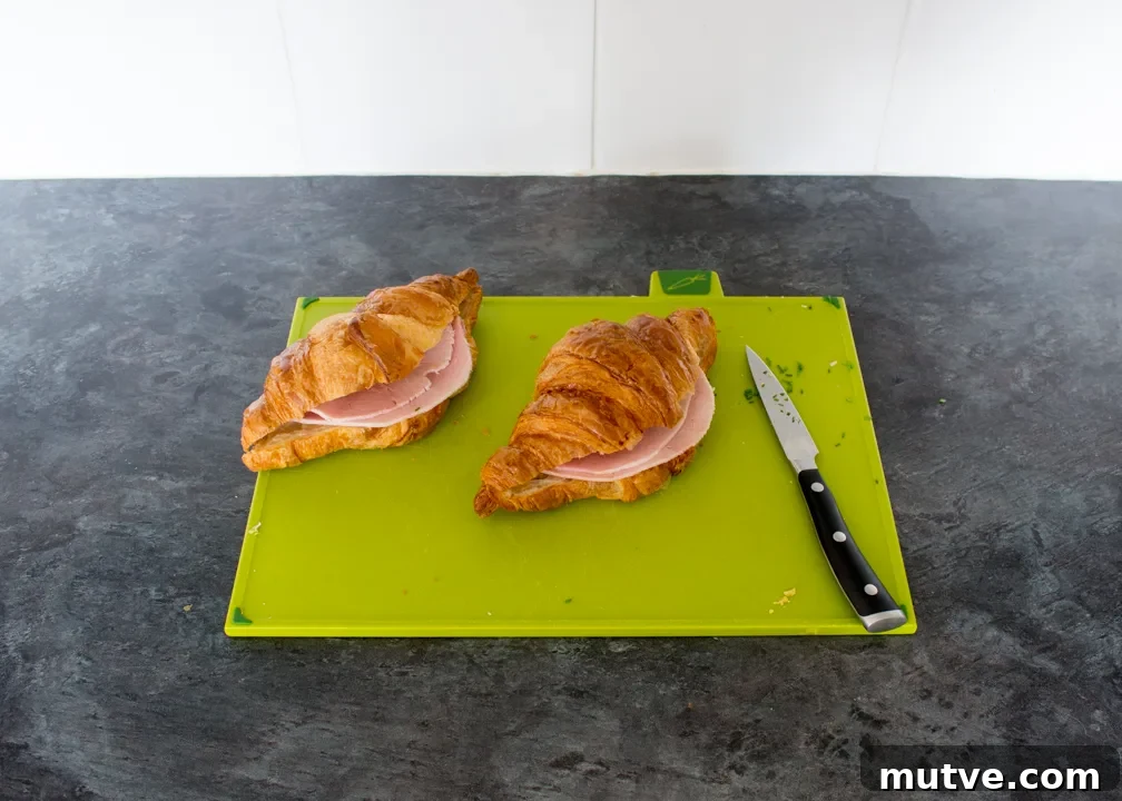 Cheese and Chive Scrambled Egg Croissant Recipe 15 Two croissants cut in half, each with a folded slice of ham inside.