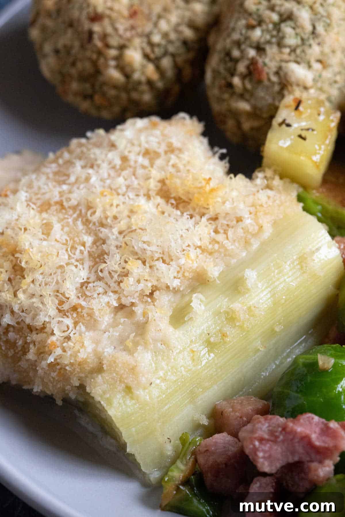 Cheesy Leek Gratin: Creamy Baked Leeks 7 Baked leeks in cheese sauce on a plate with brussels sprouts and parmentier potatoes.