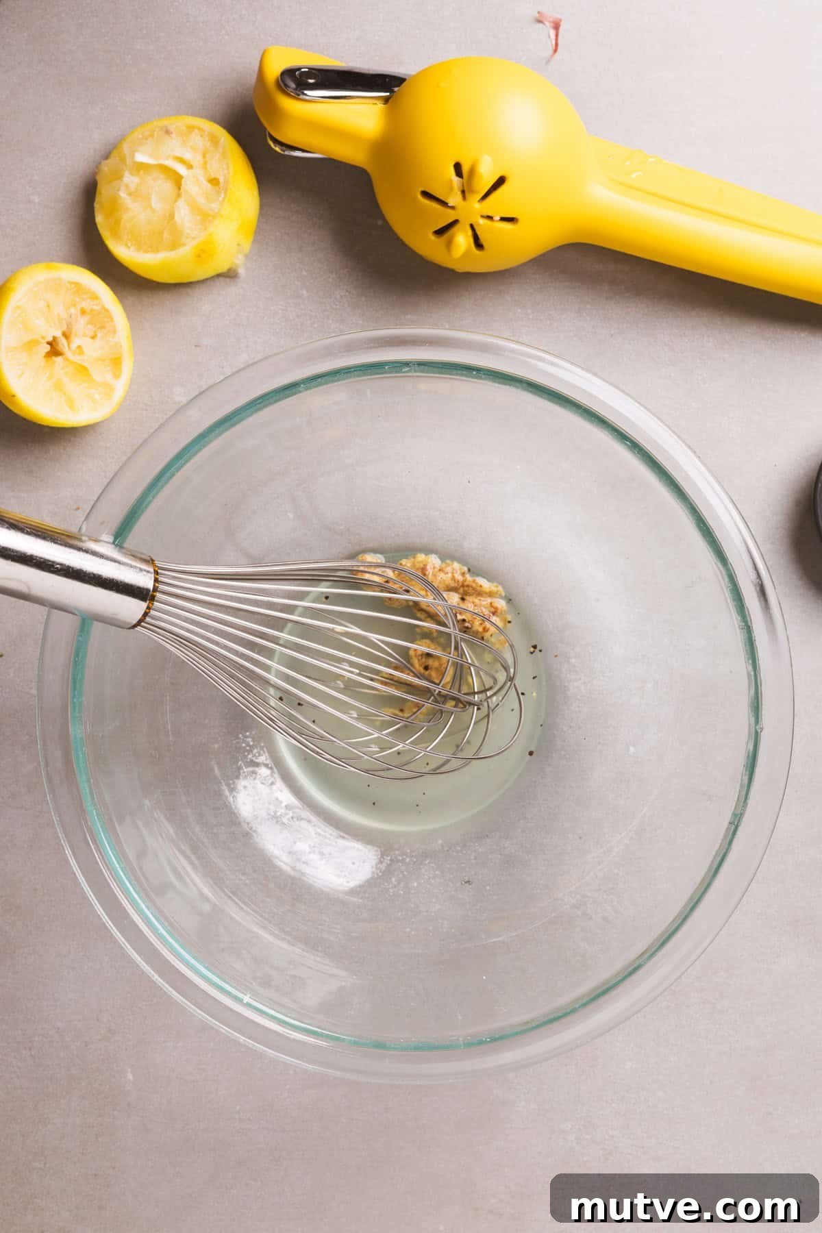 Mustard and lemon juice getting whisked together in a medium glass bowl.