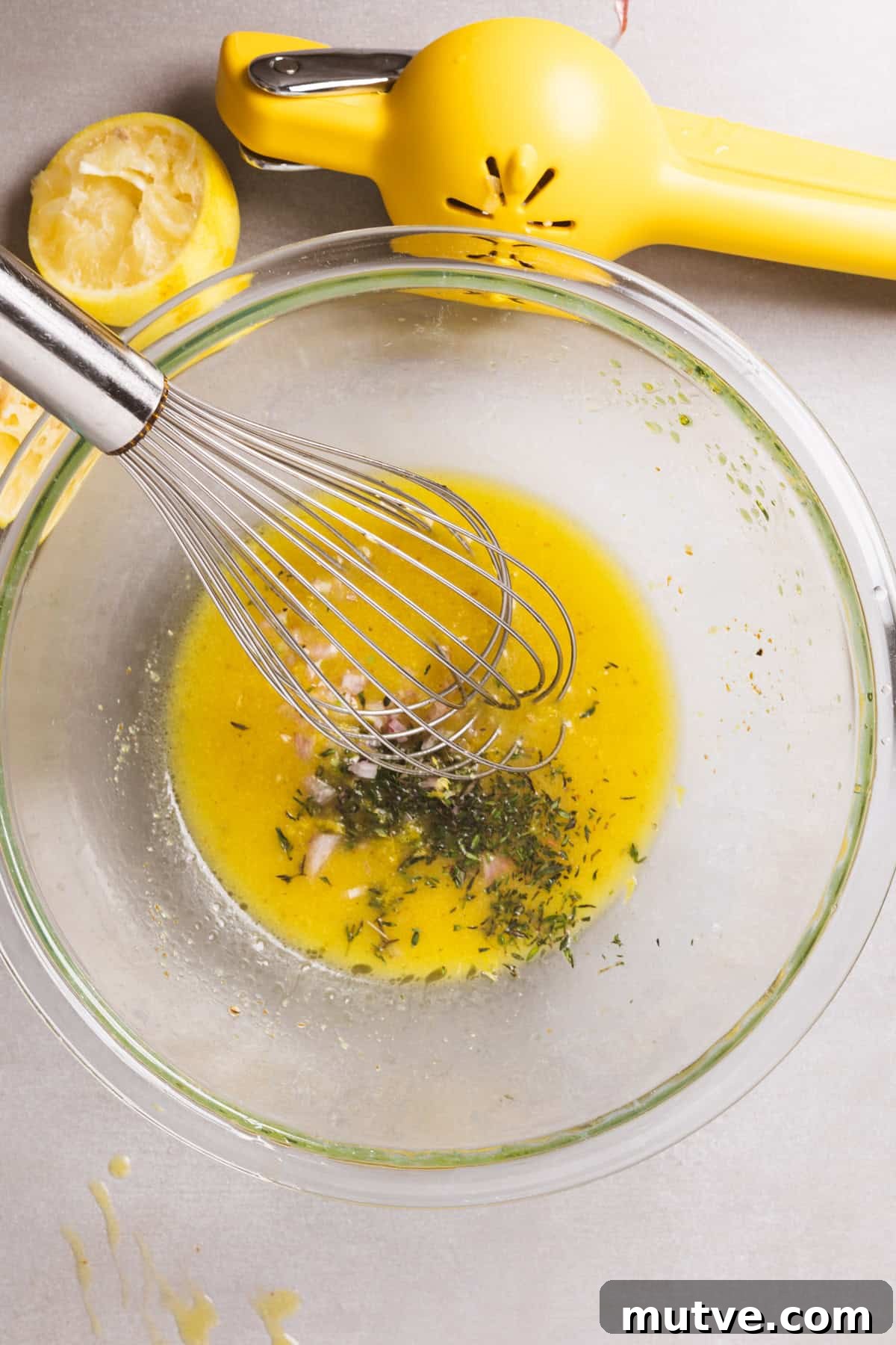 A glass bowl with a lemon vinaigrette with fresh thyme, lemon zest, and shallot getting stirred in.