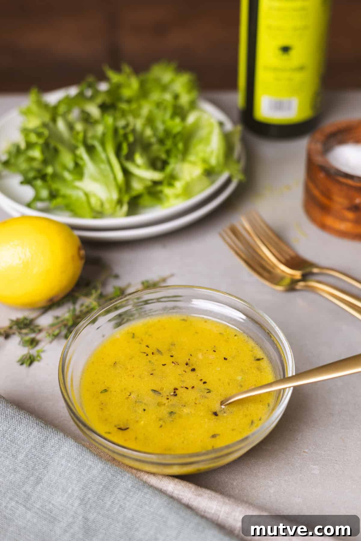 Lemon thyme vinaigrette on a gray table with a bowl of salad in the background.