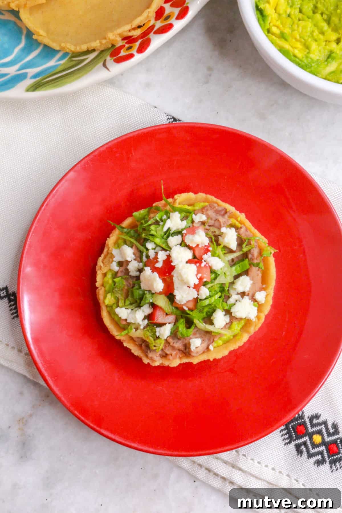 Traditional Mexican Refried Bean Sopes Recipe 12 Sopes de frijoles on a red plate with a platter of sopes behind it