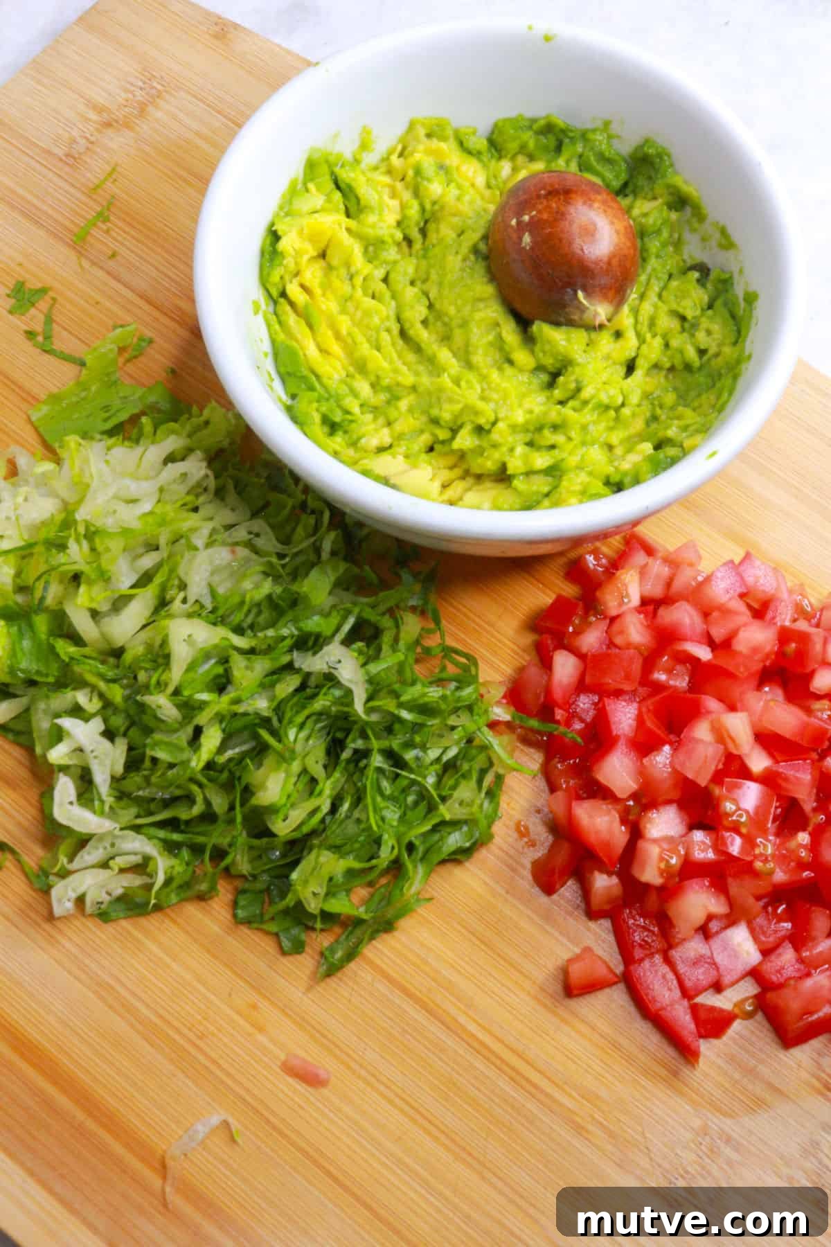 Traditional Mexican Refried Bean Sopes Recipe 5 A bowl with mashed avocado on a cutting board with shredded lettuce and diced tomato