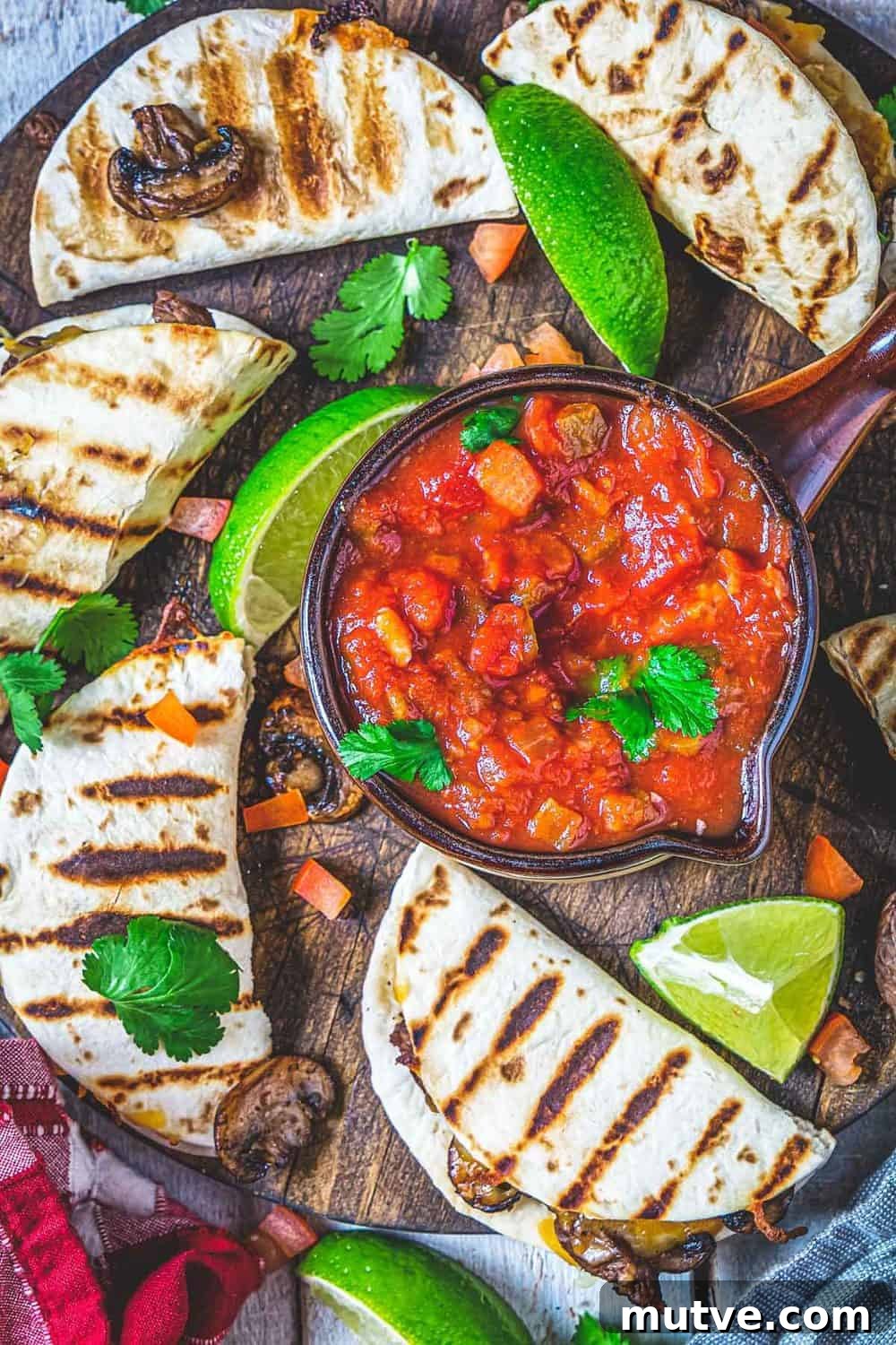 Small grilled tortillas with steak, mushrooms, and lime wedges placed around a bowl with salsa.