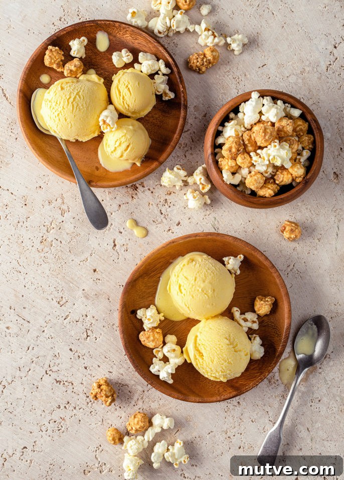 Two wooden plates with scoops of sweet corn gelato, some caramel and plain popcorn, and two metal spoons. A wooden bowl filled with mixed popcorn is also shown. Popcorn is scattered on the beige surface. // FoodNouveau.com