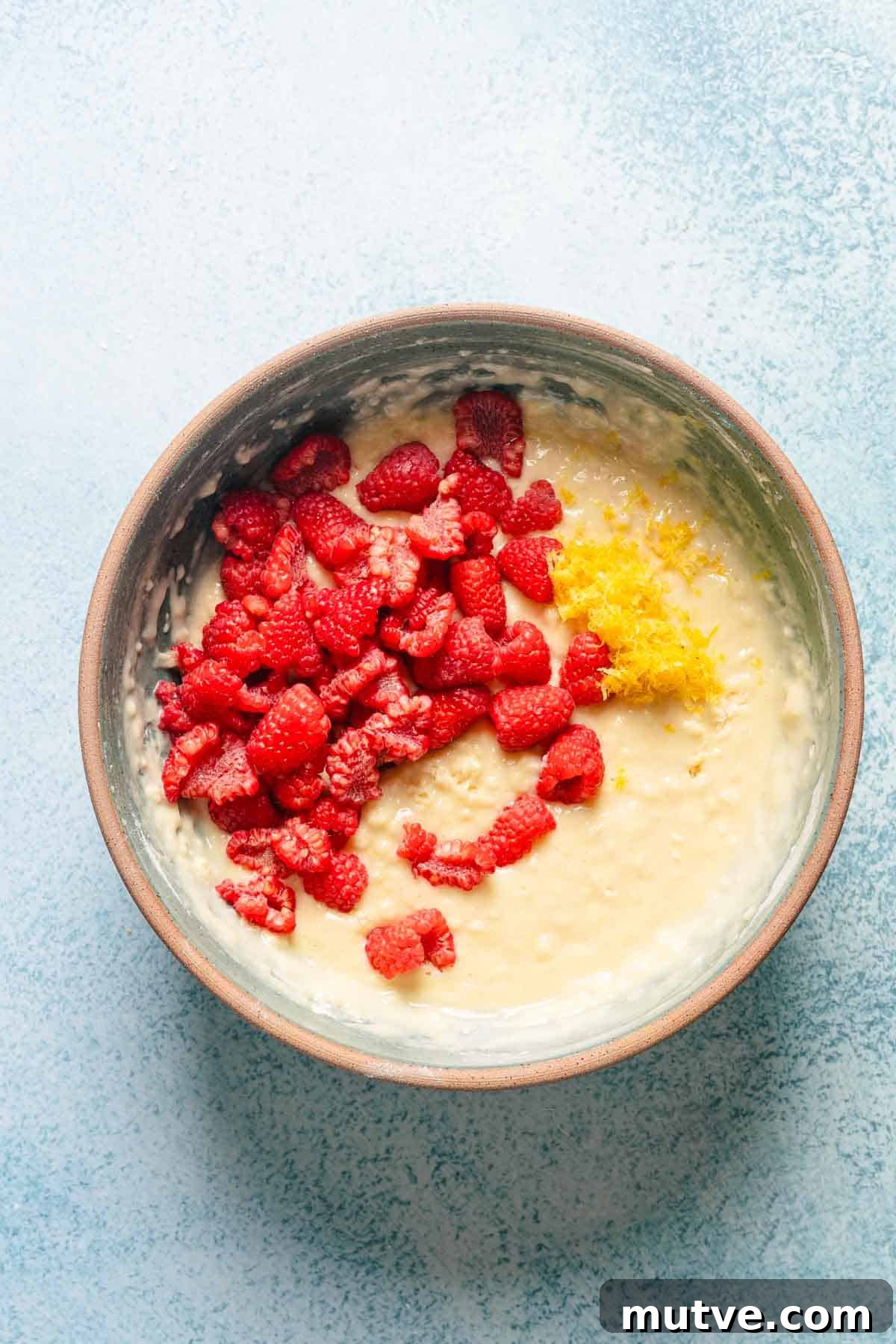 raspberries and lemon zest on top of cake batter in bowl.