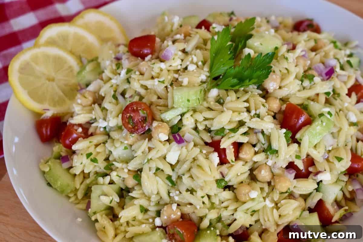 Lemon Orzo Salad Recipe with Feta and Fresh Herbs 5 Lemon orzo salad in a white bowl with lemon slices next to it.