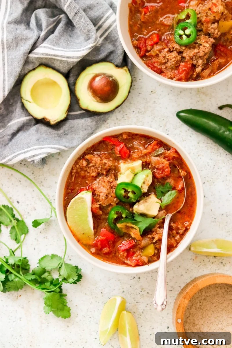 a bowl of chili topped with avocado, jalapeno, and lime.
