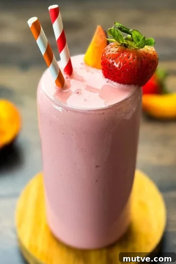 Strawberry peach smoothie in a tall glass garnished with fresh strawberry slices and peaches.