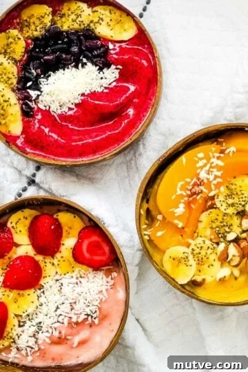 Three thick smoothie bowls topped with strawberries, bananas, blueberries, peaches, coconut, chia seeds, and almonds.