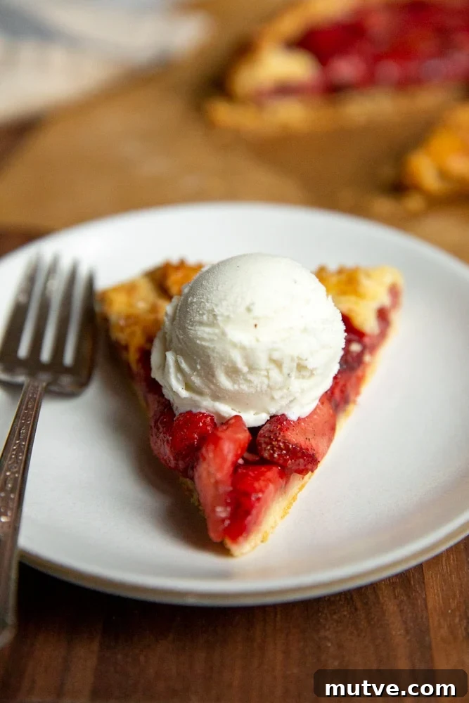 A slice of galette on a plate, topped with a scoop of vanilla ice cream.