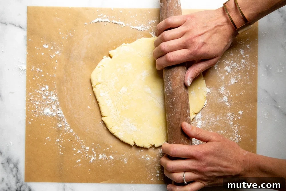 Process shot showing hands rolling out a piece of pie dough.