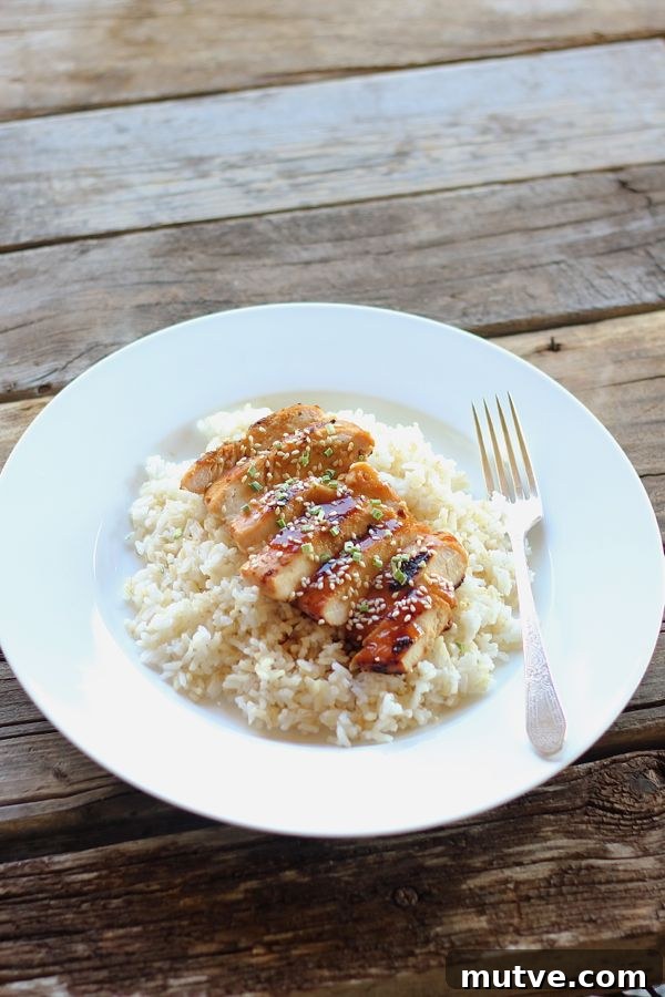 Homemade Teriyaki Chicken sliced and served over rice on a plate with a fork.