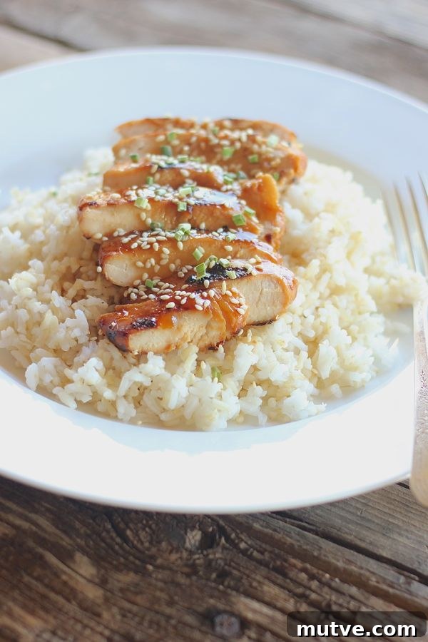 Homemade Teriyaki Chicken sliced and served over rice on a plate with a fork.