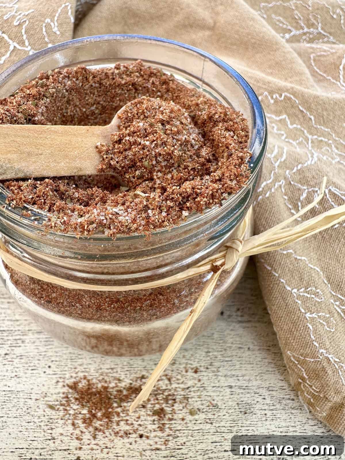 A small jar full of taco seasoning with a spoon on top and a napkin.