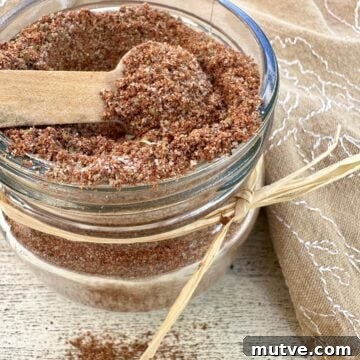 A small jar full of taco seasoning with a spoon on top and a napkin.