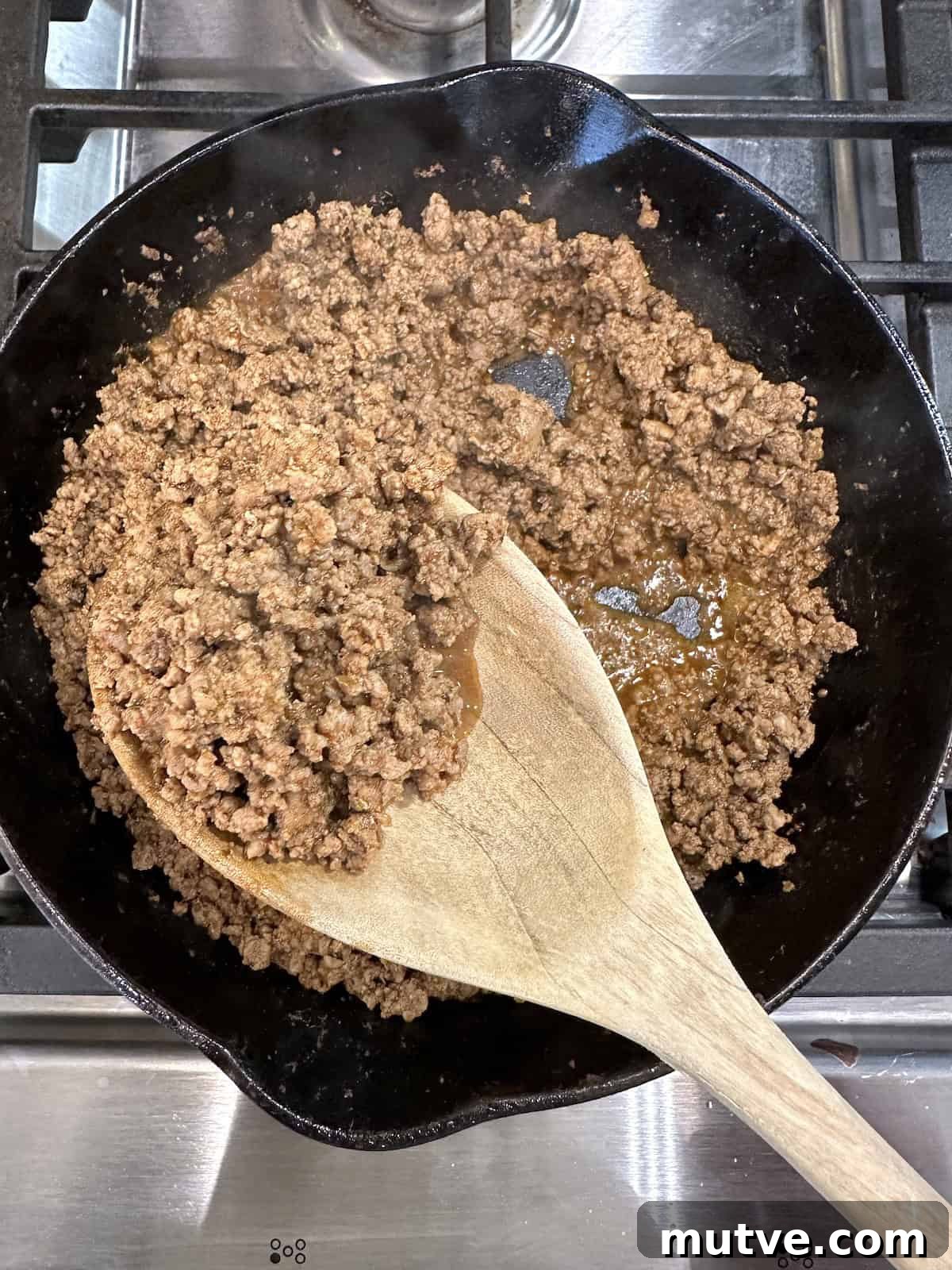 Cooked beef with taco seasoning in a skillet with a spoon.