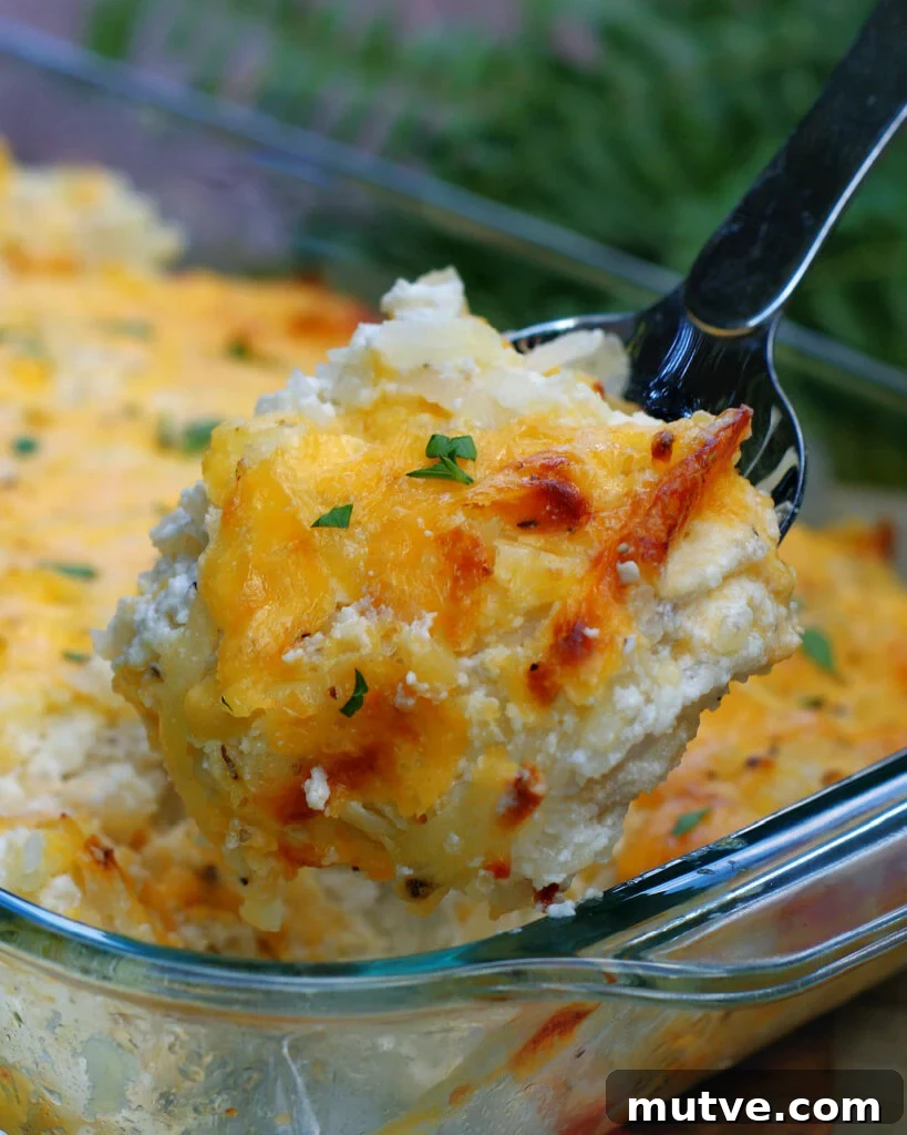 Serving a spoonful of this creamy hash brown casserole topped with melted sharp cheddar cheese.