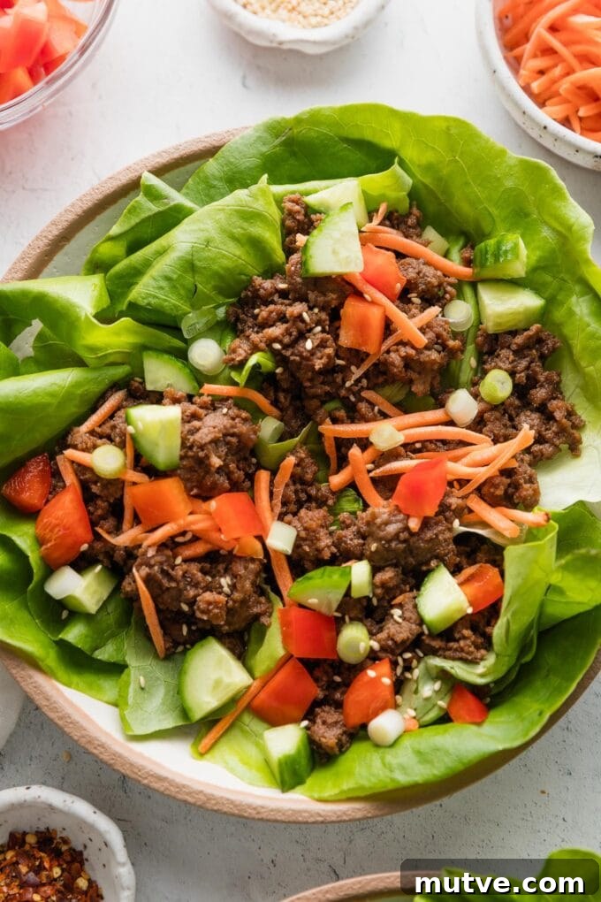 Korean Beef Lettuce Wraps Recipe with Gochujang Glaze 2 Small plate filled with three Korean beef lettuce wraps topped with fresh carrots, cucumber, bell pepper, green onions, and toasted sesame seeds.