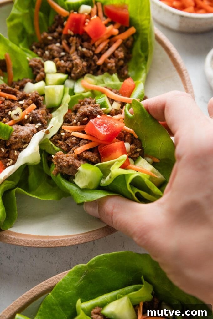 Korean Beef Lettuce Wraps Recipe with Gochujang Glaze 3 A woman's hand picking up a lettuce wrap from a plate.
