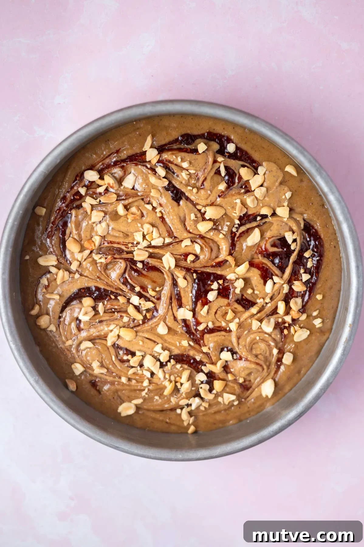peanut butter and jelly swirl with peanuts over cake batter in a baking pan