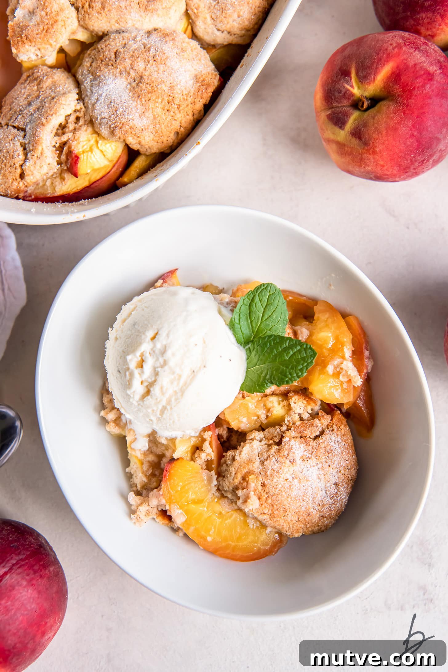 peach cobbler serving in a bowl with scoop of vanilla ice cream next to fresh peaches