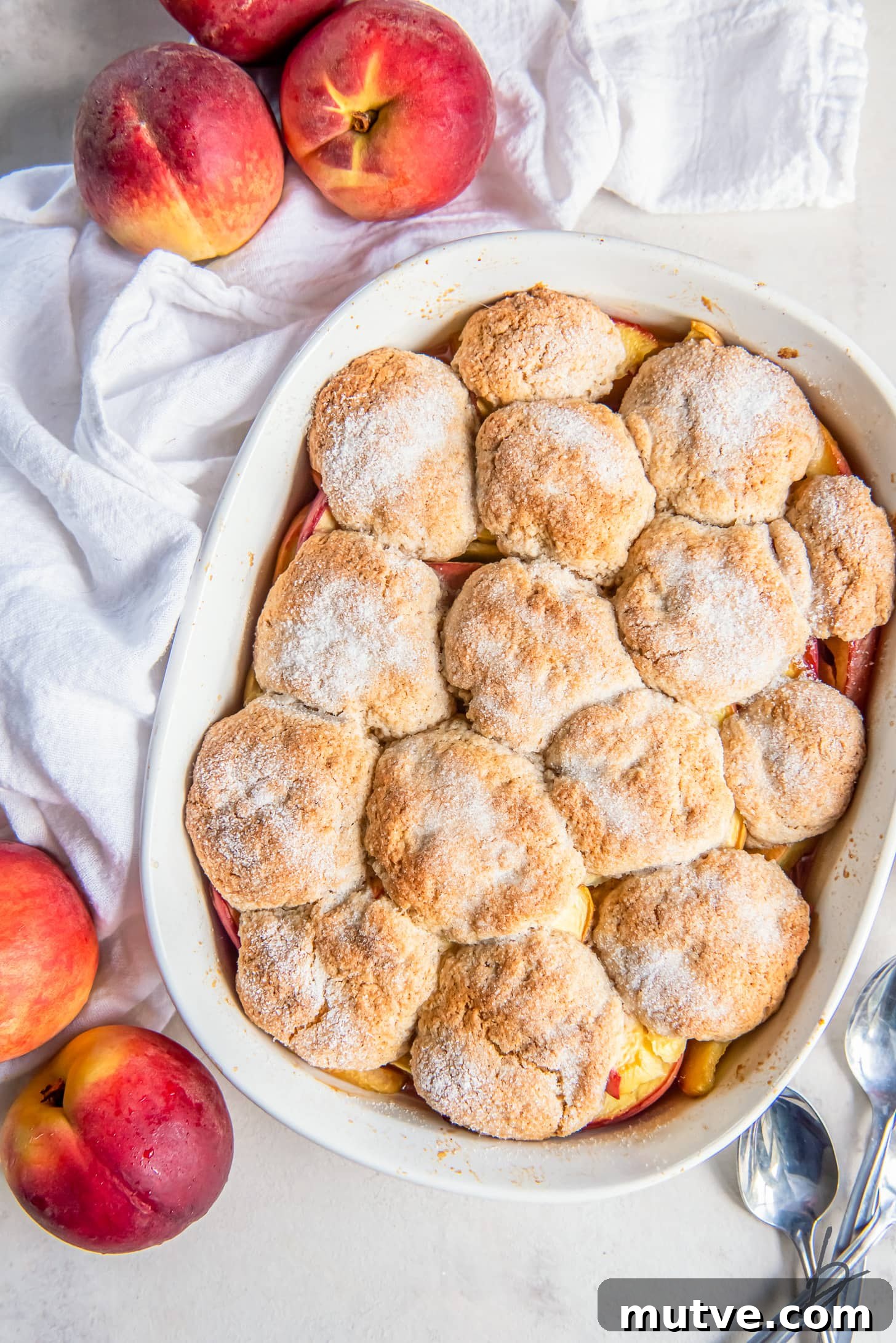 homemade peach cobbler in a baking dish with sugar sprinkled on top of baked biscuit topping