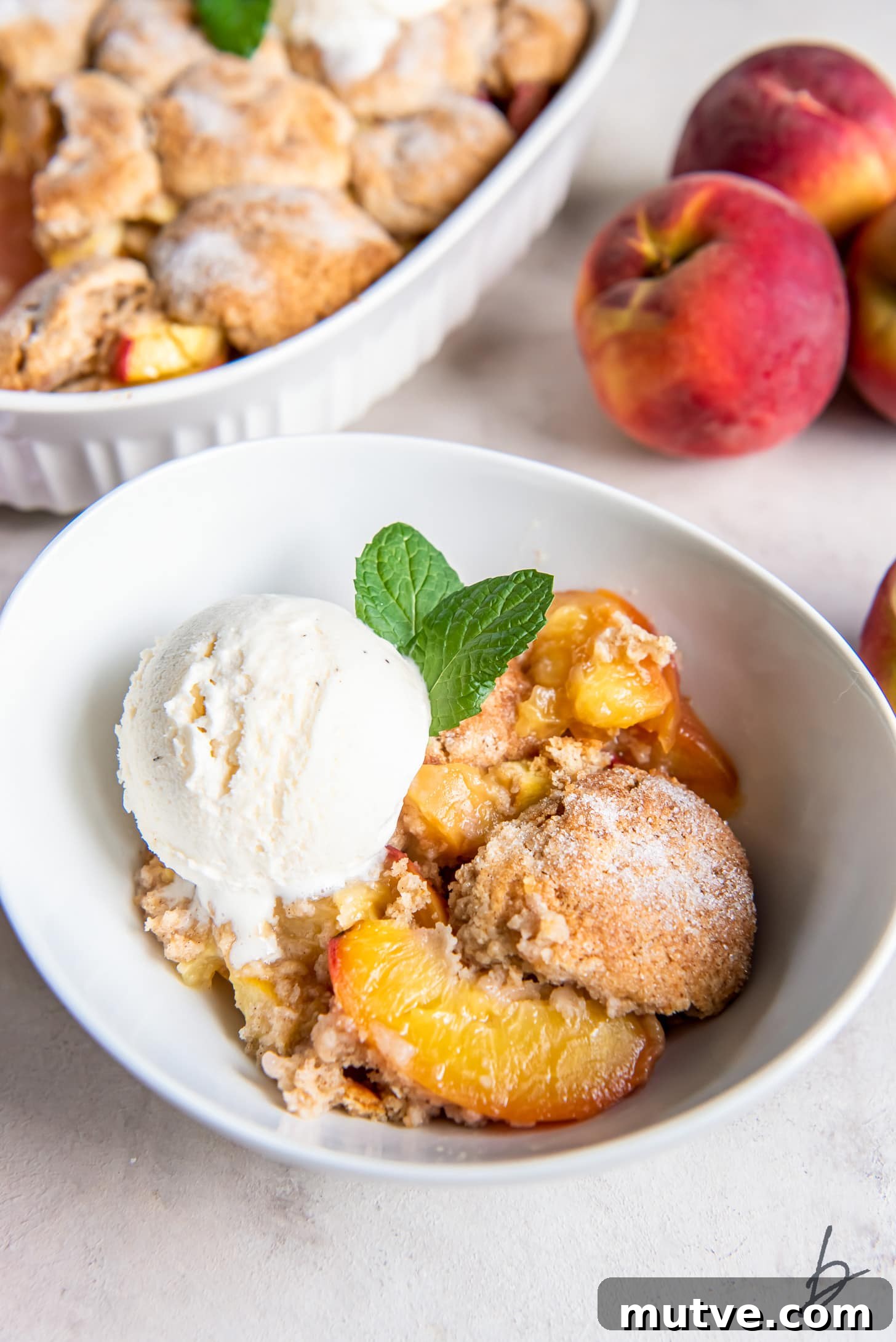peach cobbler servings in a bowl topped with a scoop of vanilla ice cream and sprig of mint