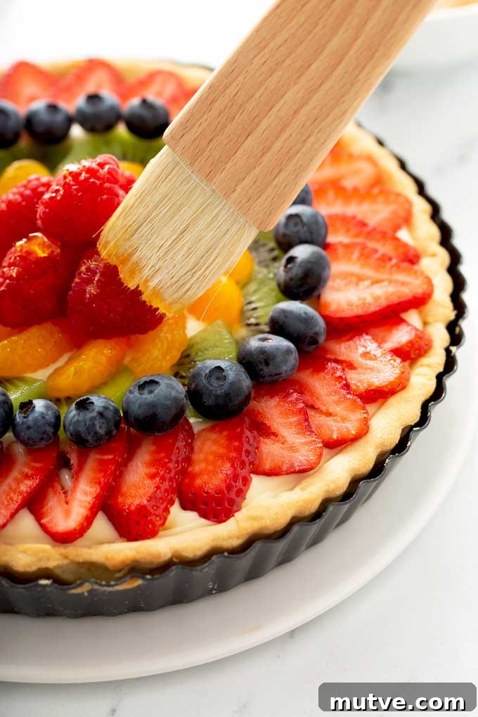 How to Make a Fresh Fruit Tart with Vanilla Custard 8 Fruit getting dub with tart glaze with a pastry brush.