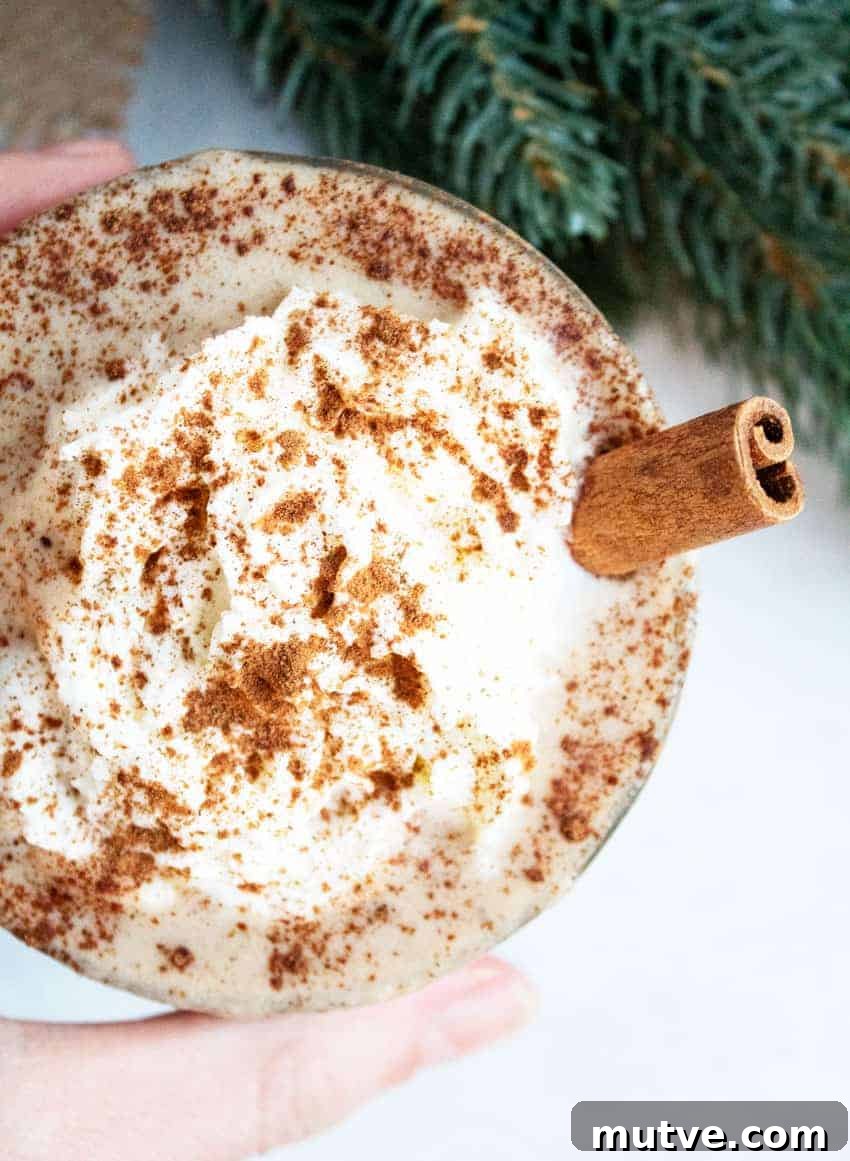 hand holding a glass of keto eggnog next to greenery
