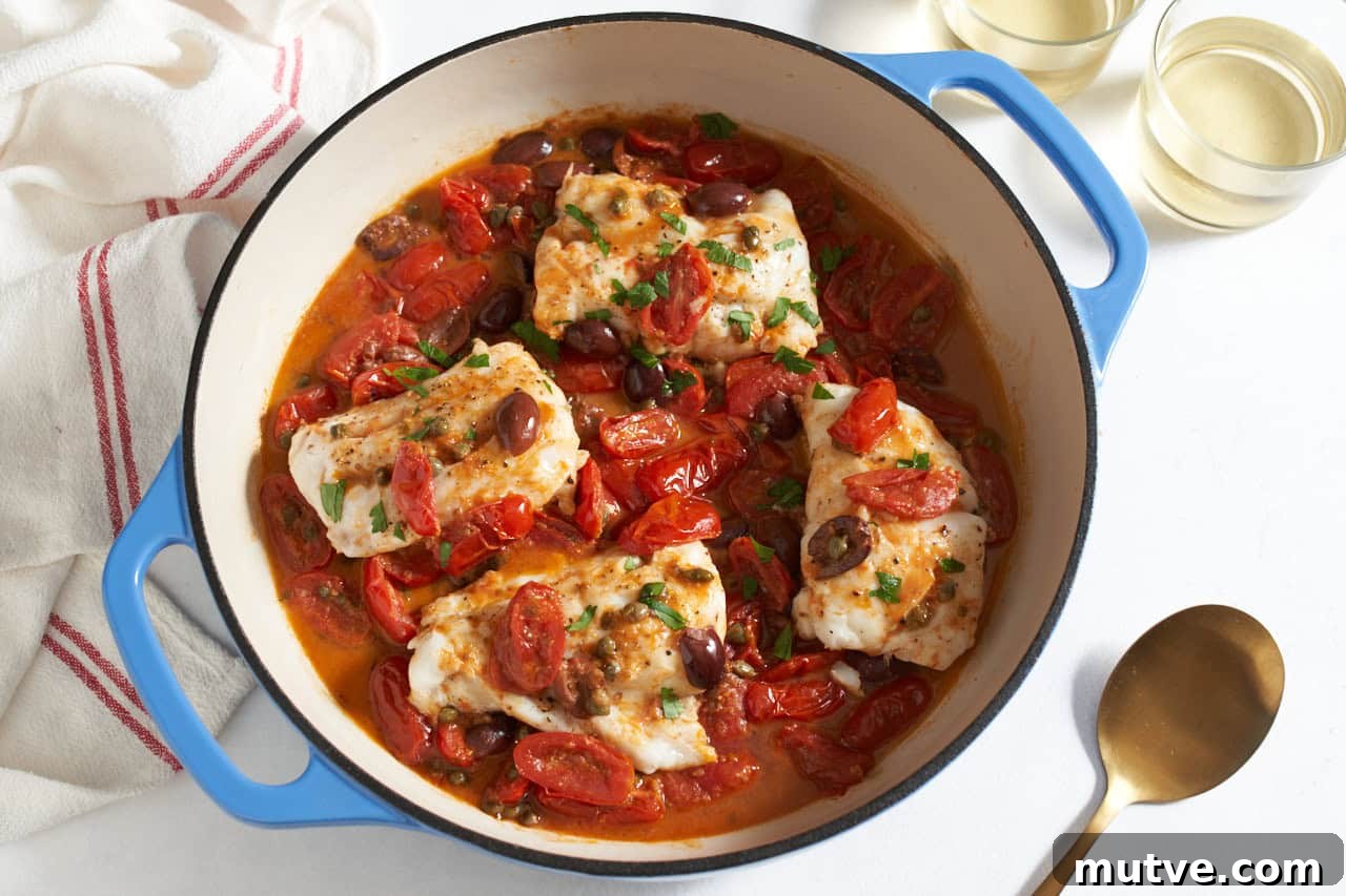 One-Pan Puttanesca Fish Recipe 2 Fish puttanesca in a skillet with blue handles, a gold spoon and two glasses of white wine are on the right.
