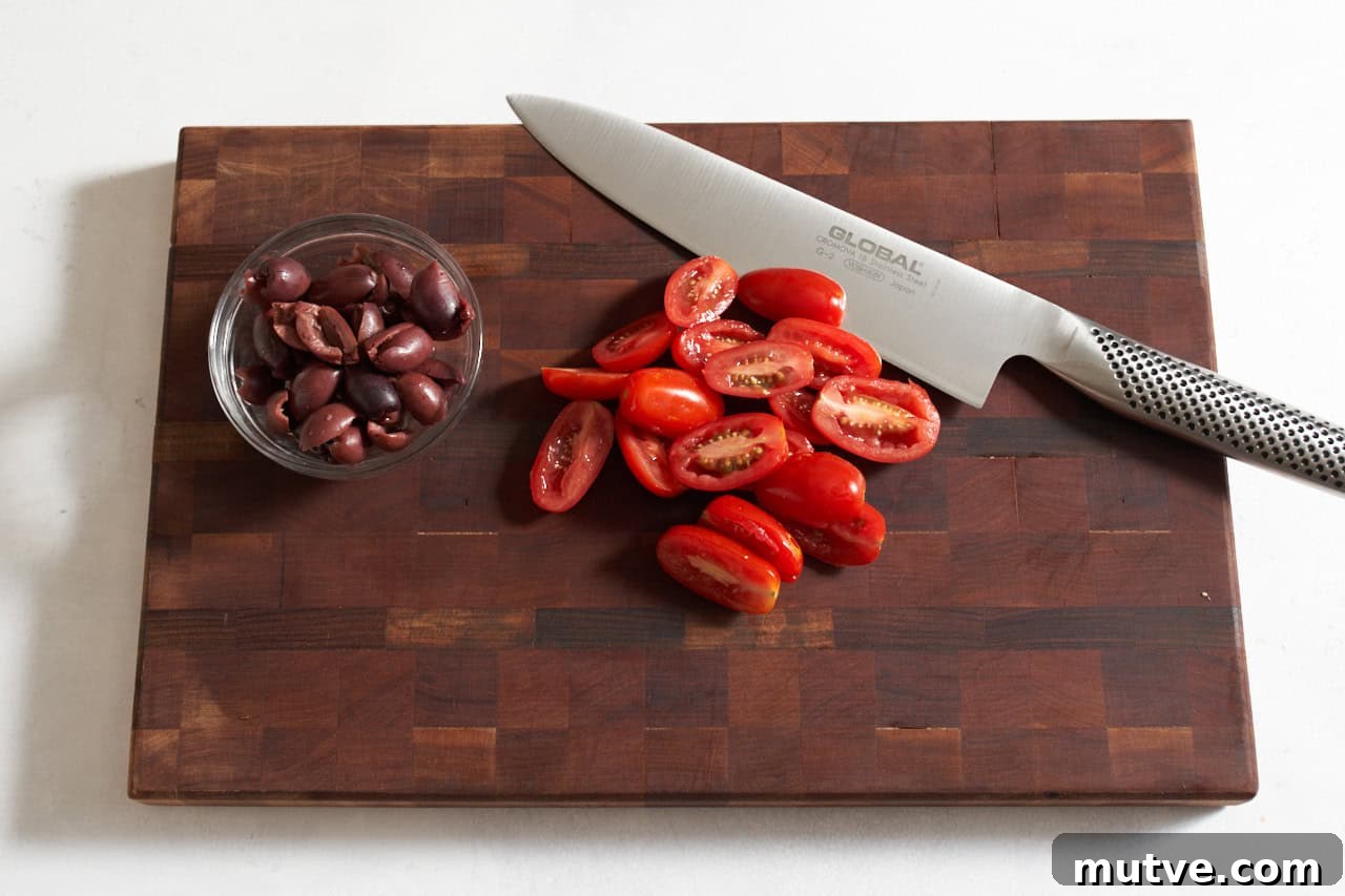 One-Pan Puttanesca Fish Recipe 4 Sliced grape tomatoes and a bowl of halved kalamata olives on a wooden cutting board with a knife.
