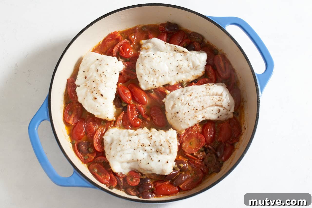 One-Pan Puttanesca Fish Recipe 6 Fish filets added to puttanesca sauce in a skillet with blue handles.