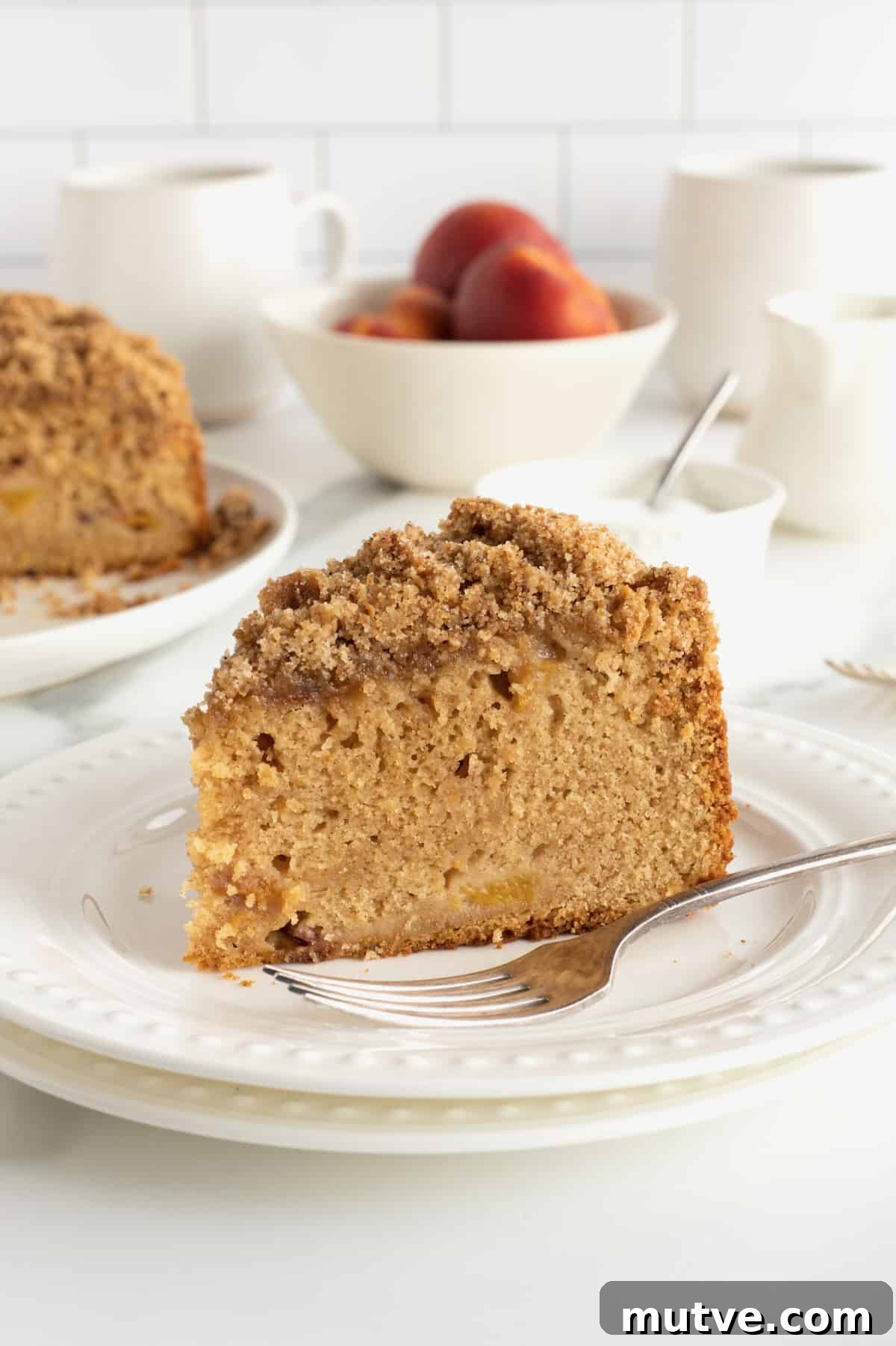 Peach Coffee Cake with Cinnamon Streusel 4 A slice of peach coffee cake on a white plate with a fork.