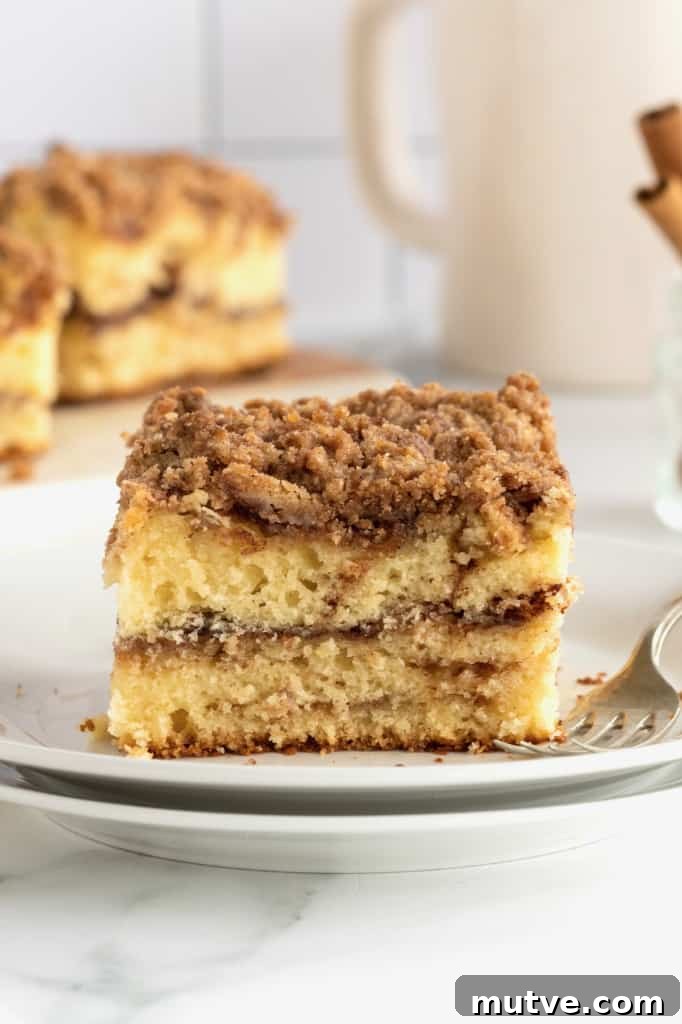 Peach Coffee Cake with Cinnamon Streusel 5 A square slice of coffee cake on a stack of white ceramic plates with a metal fork.