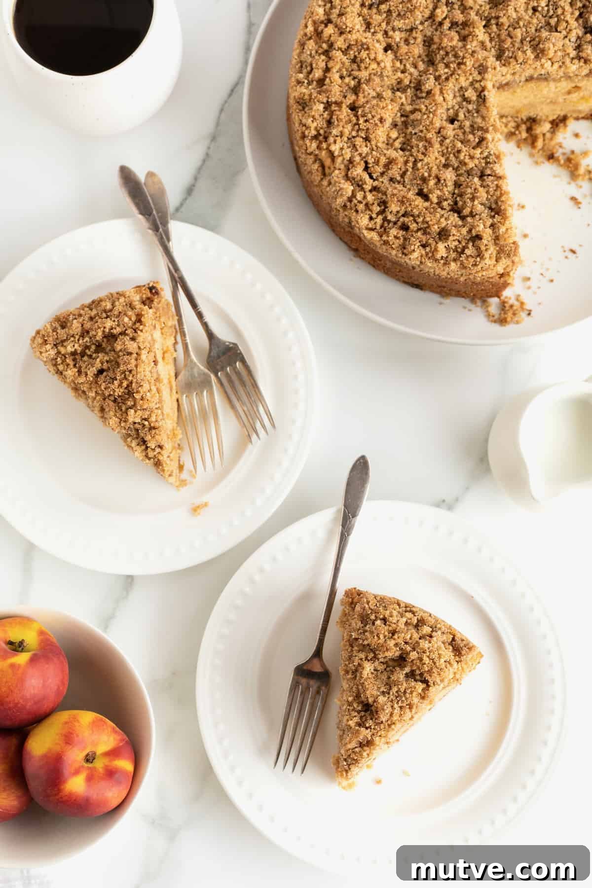 Peach Coffee Cake with Cinnamon Streusel 6 Two slices of peach coffee cake on white plates with forks and fresh peaches in the foreground.