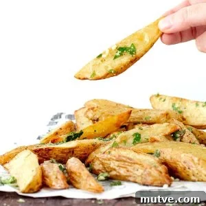 Single parsley sprinkled baked potato wedge being lifted from a pile.