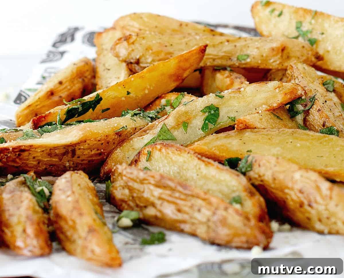 Close up of baked potato wedges with parmesan and parsley on a white and black paper.