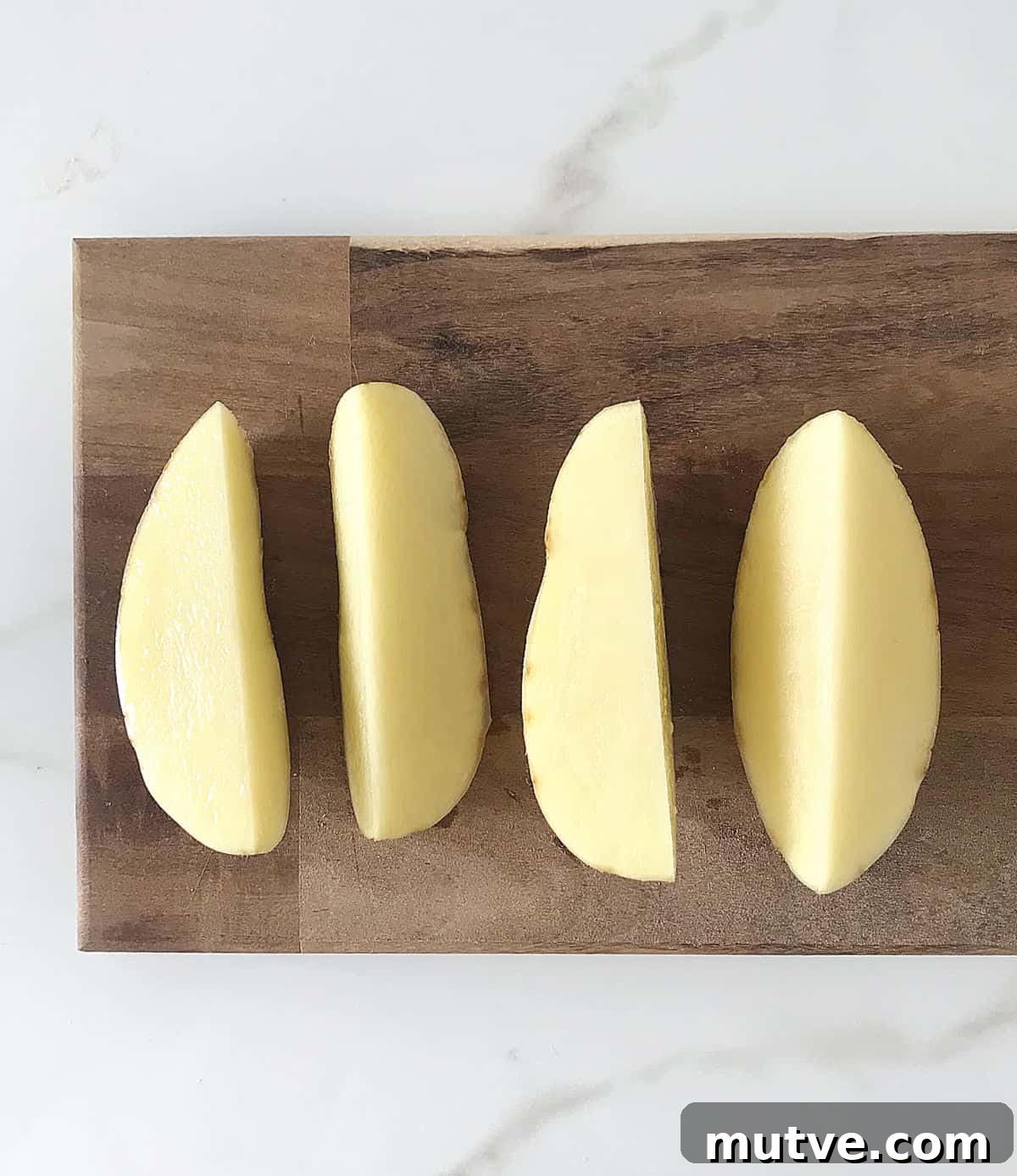 Wooden board with four raw potato wedges.