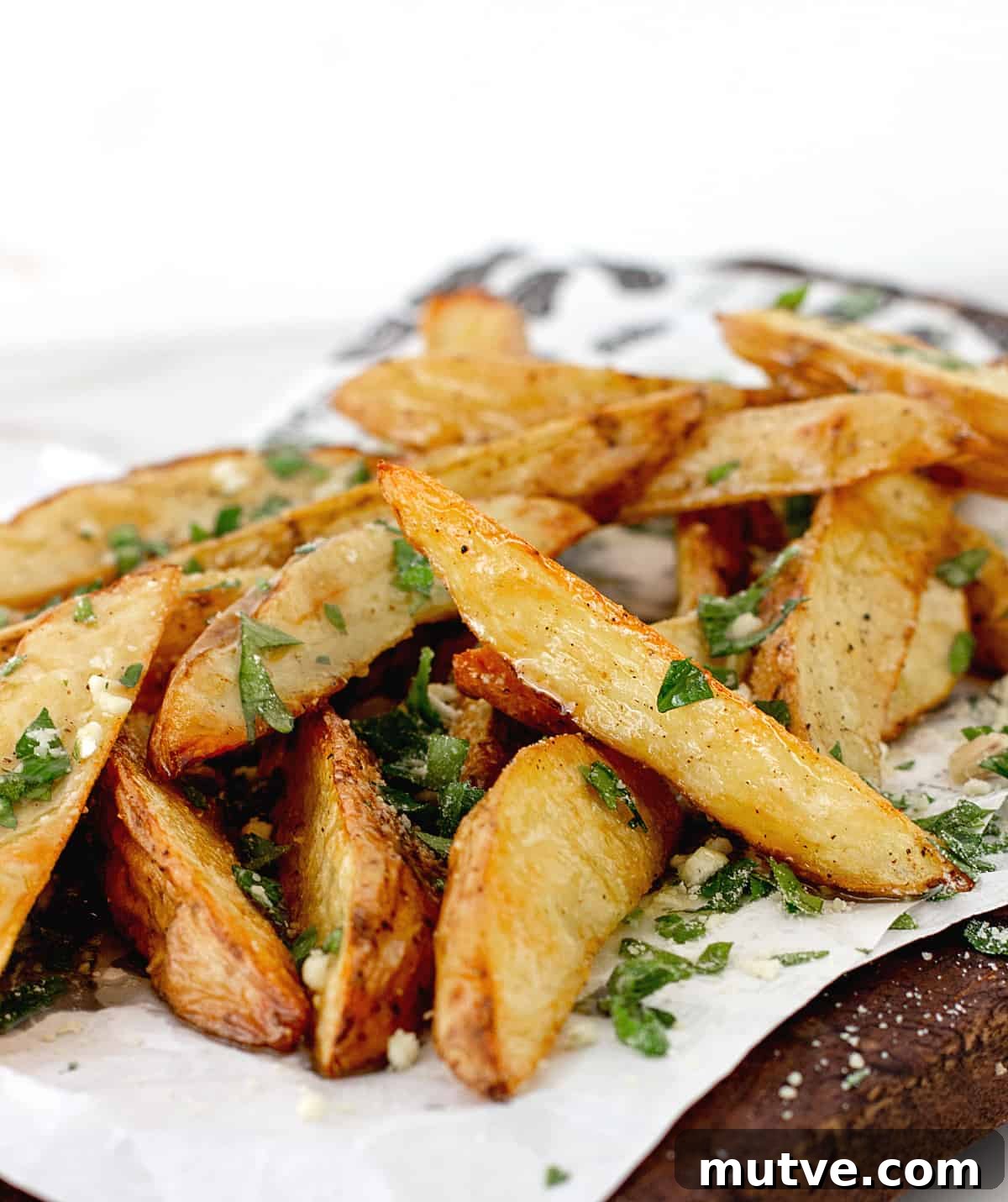 Mound of potato wedges with parsley on white paper.