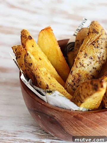 spicy baked potato wedges in wooden bowl on white table