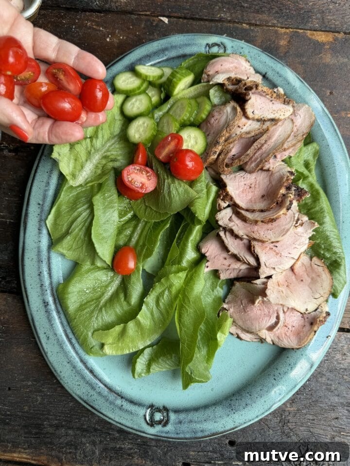 Fresh mixed greens and cherry tomatoes with sliced pork tenderloin on a blue plate.