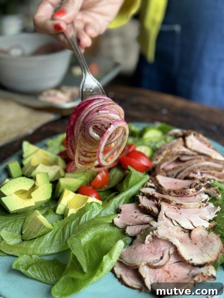 Freshly sliced roast pork with vegetables and salad greens on a plate, perfect for a healthy meal.