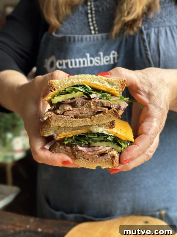 two pork tenderloin sandwich halves with arugula cheese and onions on a sandwich bread stacked by two hands with red nail polish
