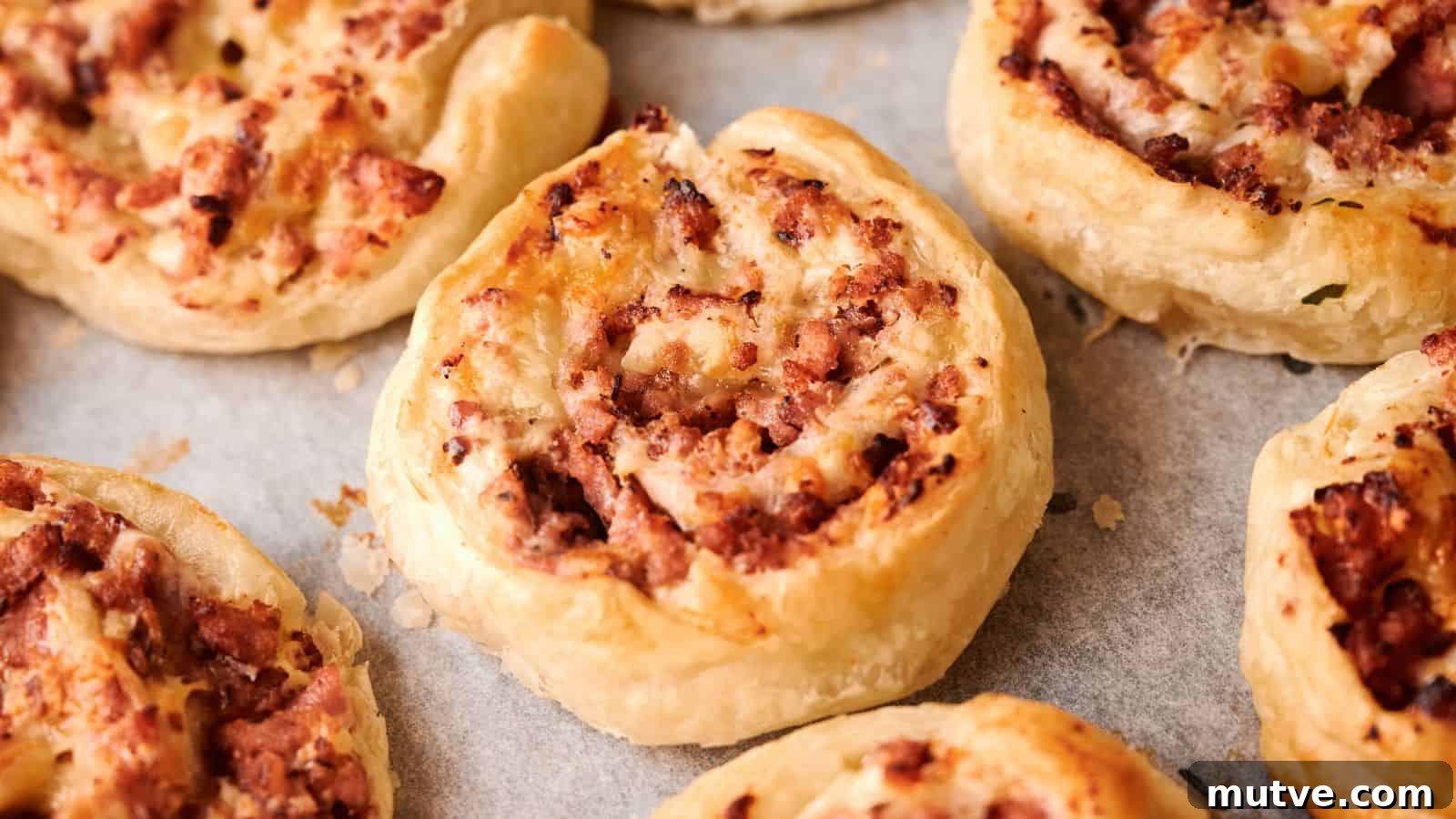 Close-up of several baked puff pastry pinwheels filled with minced meat, arranged on a baking tray lined with parchment paper.